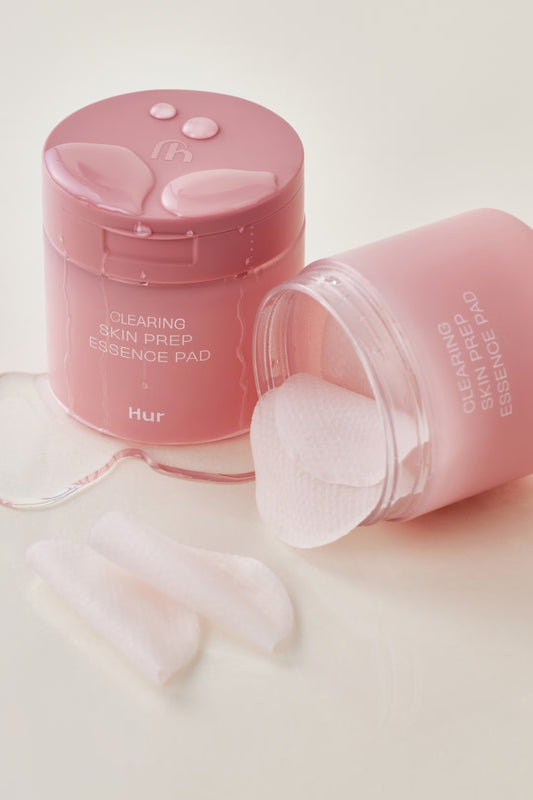 Pink 'Clearing Skin Prep Essence Pad' container with pads on a light pink background