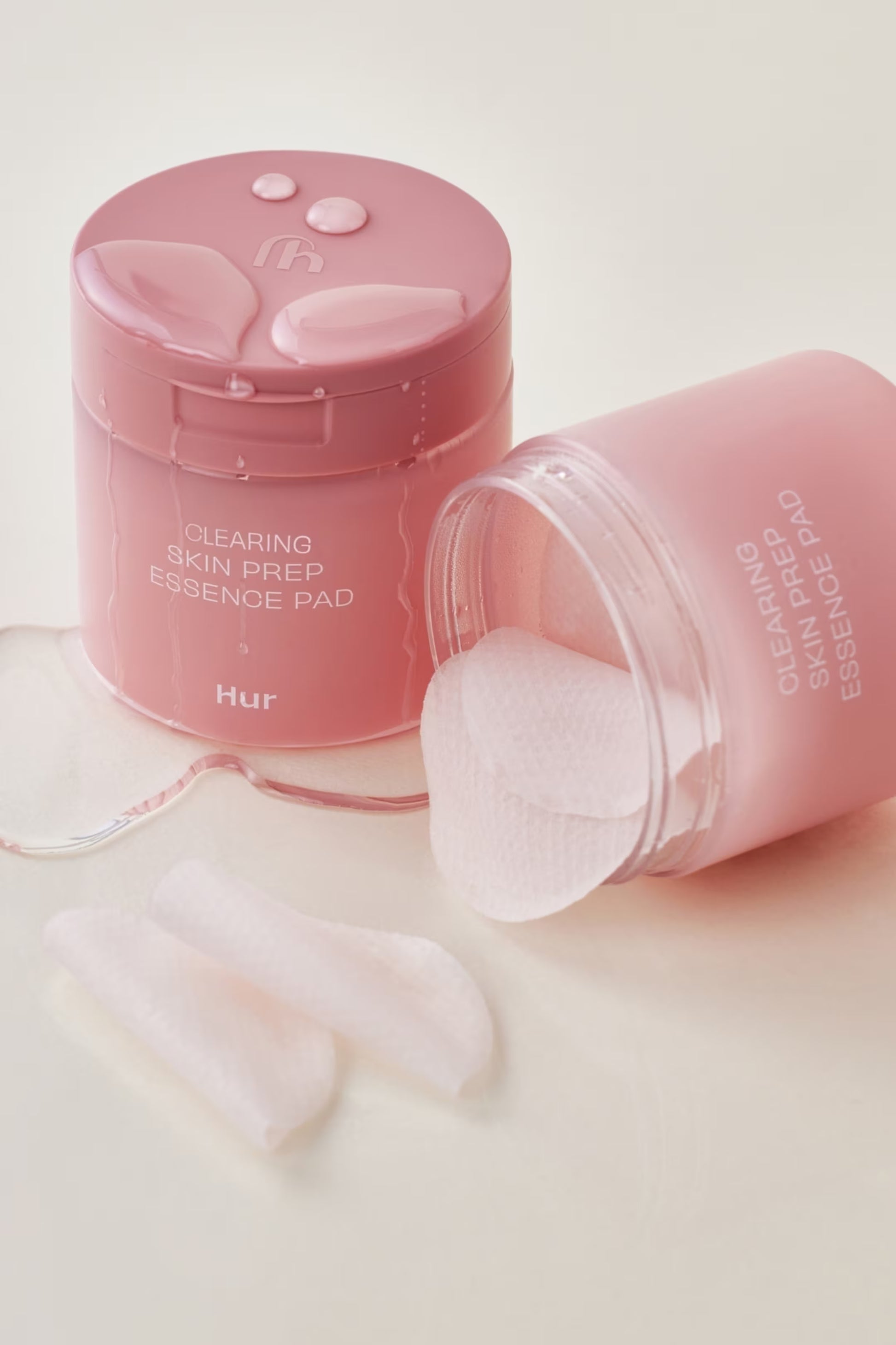 Pink 'Clearing Skin Prep Essence Pad' container with pads on a light pink background